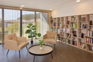une bibliothèque avec deux chaises, une table et des étagères dans l'établissement Zenitude Hôtel-Résidences Saint-Paul-lès-Dax, à Saint-Paul-lès-Dax