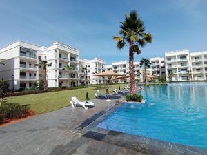 a swimming pool with a palm tree and some buildings at Charming appartement in Bouznika in Bouznika