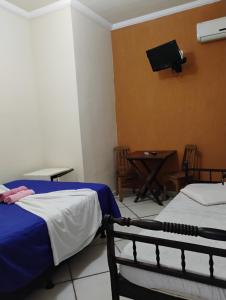 a room with two beds and a table and a tv at Pousada Pé na Praia in Rio das Ostras