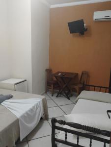 a room with two beds and a table and a tv at Pousada Pé na Praia in Rio das Ostras
