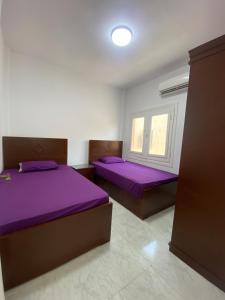 two beds in a room with purple sheets and a window at Twin Villa with Private Garden & Rooftop at Orchidia Village Sidi Abdelrahman in El Alamein