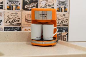 an orange coffee maker with two white coffee mugs at Flat Pinheirinho in Capitólio