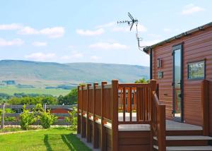 a wooden cabin with a deck and mountains in the background at Wild Rose Holiday Park in Colby