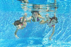 a man and two children swimming in a swimming pool at Caravan With Large Decking At Coopers Beach Holiday Park Ref 49012Sv in East Mersea