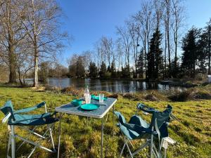 a picnic table with three chairs in the grass near a river at Les Rives De Bel Air - Hébergements - Camping - Caravaning in Saint-Siméon
