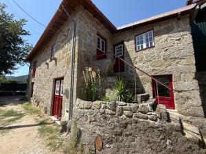 an old stone house with red doors and a stone wall at Refúgio Rural - Gerês in Terras de Bouro