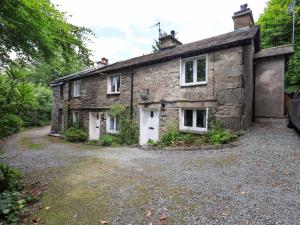 an old stone house sitting on a gravel driveway at Fellside Cottage in Bowness-on-Windermere