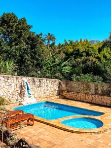a swimming pool with two benches and a stone wall at Pousada Acessus - Familia, Amigos e Network in Anápolis