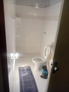 a white bathroom with a toilet and a blue rug at Suítes da Raquel Ype Amarelo in Alto Paraíso de Goiás