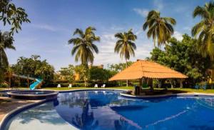 a swimming pool with an umbrella and palm trees at Villa Hotel Puerta del Mar in Ixtapa
