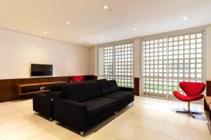 een woonkamer met een zwarte bank en een rode stoel bij Condôminio Latitude 23 - Ubatuba in Ubatuba