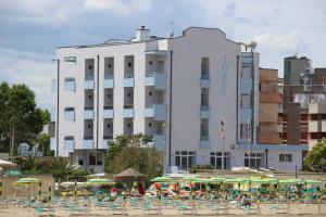 un gran edificio blanco con sillas y sombrillas en la playa en Hotel Iones, en Rímini