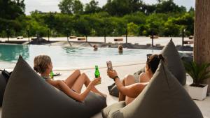 two women sitting on pillows by a swimming pool at The Farm Nusa Party Hostel in Nusa Penida