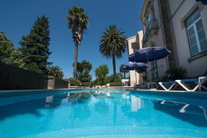 a swimming pool with chairs and an umbrella and palm trees at Hotel Sol e Serra in Castelo de Vide