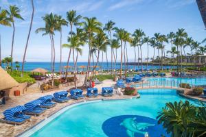 a pool at the resort with blue chairs and palm trees at SOAK UP THE SUN VILLA Sun-Drenched 3BR KaMilo Home with Golf Course View in Waikoloa