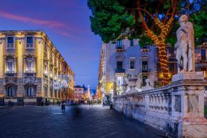 a city street at night with buildings and a statue at Carmela Homes & Residences in Catania