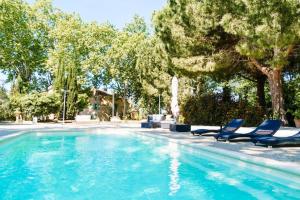 a swimming pool with two blue chairs and trees at Le Relais De Pigasse in Ouveillan