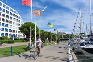 a man riding a bike down a sidewalk with flags at Le Cosy Les Pieds Dans L'eau in Le Grau-du-Roi
