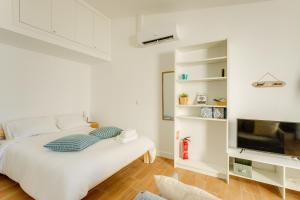 a white bedroom with a bed and a television at Charming Aroeira Beach Studio in Aroeira