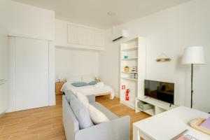 a white living room with a couch and a tv at Charming Aroeira Beach Studio in Aroeira