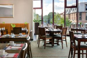 ein Restaurant mit Tischen und Stühlen und großen Fenstern in der Unterkunft Rugs Hotel Augsburg City in Augsburg