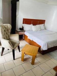 a bedroom with a bed and a chair and a table at Abuja Bays Garden Hotel Ltd in Mama