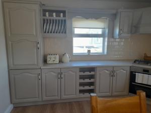 a kitchen with white cabinets and a window at Crowe's Bridge House in Quilty