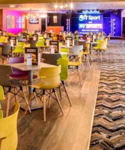 a room filled with tables and chairs with yellow chairs at The Victory Vermont in Leysdown-on-Sea