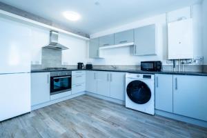 eine weiße Küche mit weißen Schränken und einem Geschirrspüler in der Unterkunft Two-bed Ground Floor Flat in Caerphilly Town Centre in Caerphilly + 5 Fotos