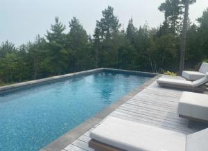 a swimming pool with two lounge chairs on a wooden deck at Domaine Fairbanks in La Malbaie