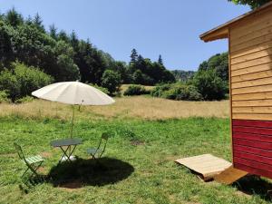 a table and chairs with an umbrella in a field at Roulotte au pied des volcans, cuisine et sdb de plein air in Orcines