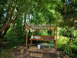 a wooden table with a wooden pergola in a forest at Roulotte au pied des volcans, cuisine et sdb de plein air in Orcines