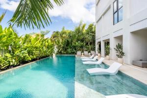 an infinity pool with white chairs and a building at Sunny Muse by Betterplace in Canggu