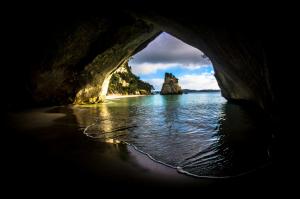 a cave entrance to a beach with a rock in the water at Whitianga Coastal Stay, Cosy Studio at Oceans Resort in Whitianga +2 photos