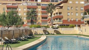 a swimming pool with chairs and umbrellas next to a building at MAR AZUL Playa y Piscina 80 metros de la playa in Roquetas de Mar +46 photos
