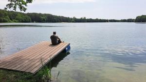a man sitting on a dock on a lake at Echo Raduni in Stężyca +3 photos