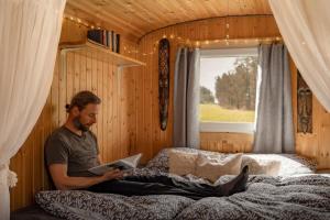 a man sitting on his bed reading a book at Maringotka Slaměnka u menhirového kruhu - U Slaměnky in Hněvětice