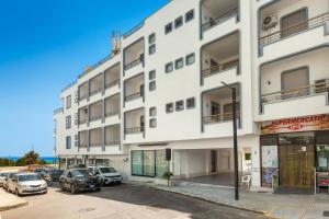 ein weißes Gebäude mit auf einem Parkplatz geparkten Autos in der Unterkunft Balconcino Vista Mare by BarbarHouse in San Foca