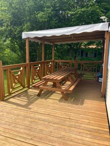 a wooden deck with a picnic table and a gazebo at Mobil-home 6 personnes bord de lac in Le Chesne