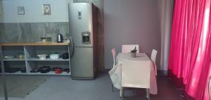 ein Kühlschrank und ein Tisch in einem Raum mit einem Tisch und rosa Vorhängen in der Unterkunft 329 on 30th Avenue Villieria Jimmy in Pretoria