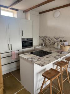 a kitchen with white cabinets and a counter with stools at Holt GRDN House A beautiful 1 bedroom house with freestanding bathtub and log burners in Holt