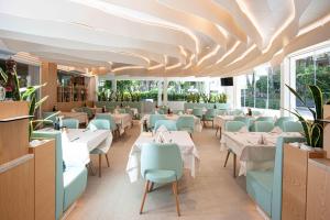a restaurant with white tables and blue chairs at Hotel Oasi in Lignano Sabbiadoro