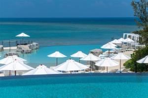 a swimming pool with white umbrellas and the ocean at Hyatt Regency Seragaki Island Okinawa in Onna