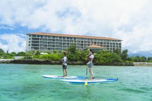 two men are standing on a paddle board in the water at Hyatt Regency Seragaki Island Okinawa in Onna
