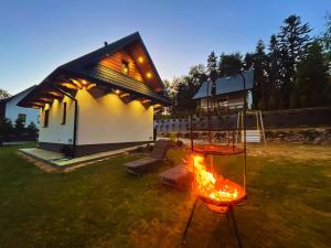 een huis met een speeltuin met een vuur in de tuin bij Biały Domek Świerczek in Słopnice