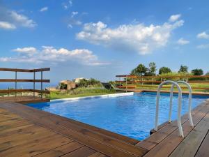 una gran piscina con una terraza de madera y un cielo azul en Terre di Monacella, en Santa Venerina