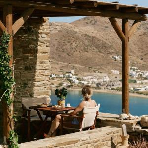 a woman sitting at a table on a patio overlooking a lake at Heliopetra Punta in Ios Chora