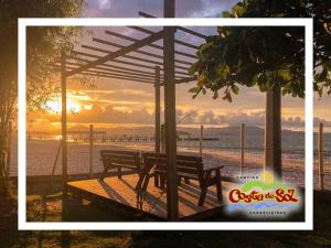 Un banco del parque con vista a la playa al atardecer. en Hospedagem em Canasvieiras - Pé na Areia com Vista para o Mar, en Florianópolis