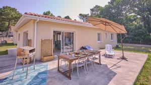 einen Tisch mit Stühlen und einen Regenschirm vor einem Haus in der Unterkunft Villa Jardin et forêt océan au Verdon in Le Verdon-sur-Mer