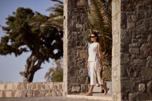 a woman in a white dress standing next to a stone wall at Hotel Milos Sea Resort in Adamantas
